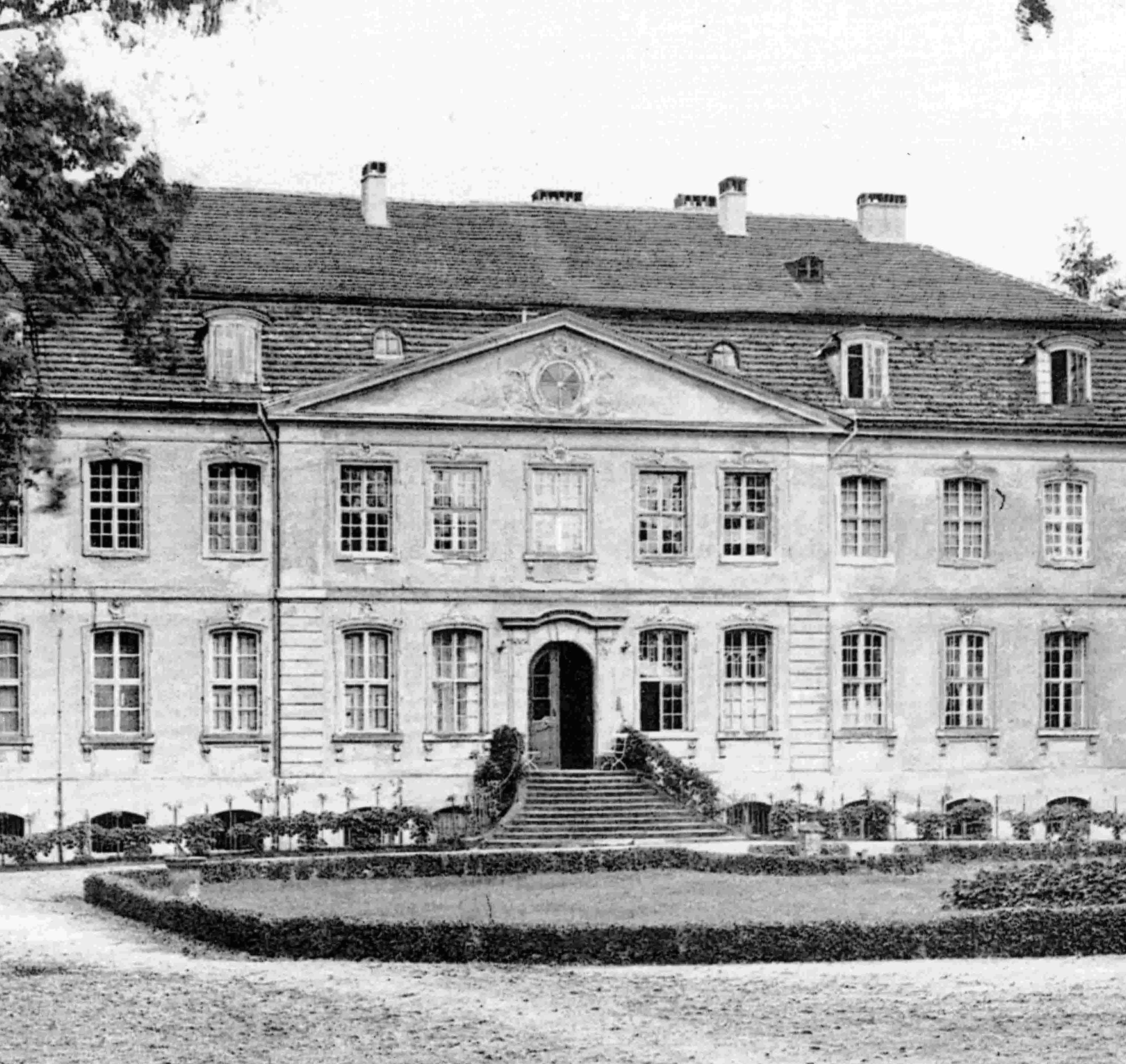 Historisches Herrenhaus umgeben von Bäumen, mit einer eleganten Fassade und einem gepflegten Garten im Vordergrund.